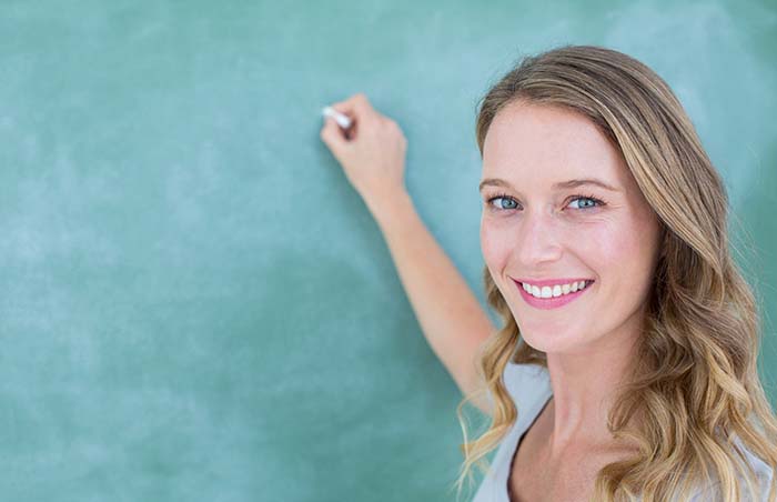 Lachende lerares schrijf op schoolbord lerares voor het schoolbord